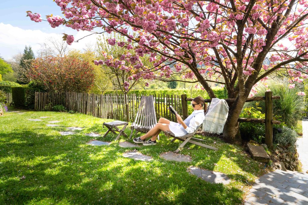 mulher a ler um livro à sombra das árvores no jardim do Auberge de la Source -auberge normandie